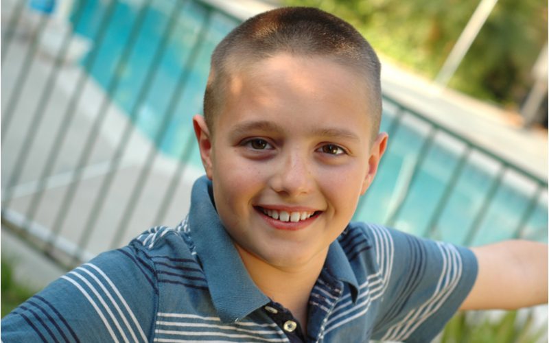 Buzzcut fade hairstyle on a kid in a dapper blue striped polo standing in front of a pool
