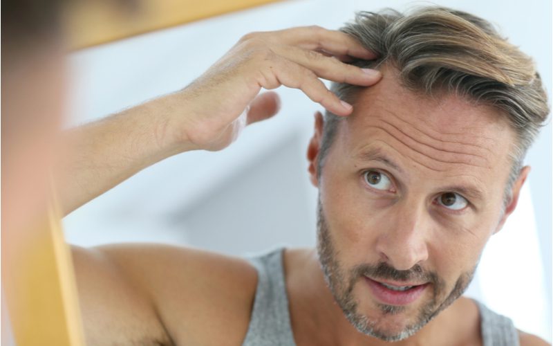 Người đàn ông lo lắng về tình trạng rụng tóc và muốn biết cách khắc phục, biểu tượng bằng việc anh ta nhìn vào gương