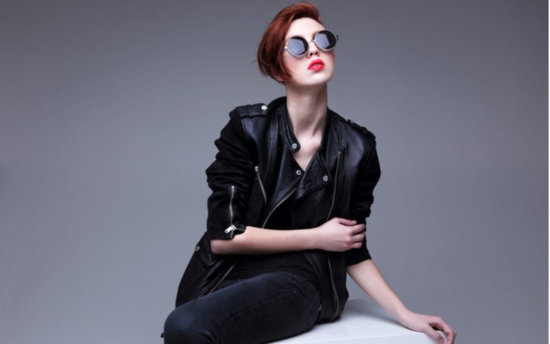 Gal with a hidden undercut bob haircut wearing a black leather jacket and dark black denim poses in a studio