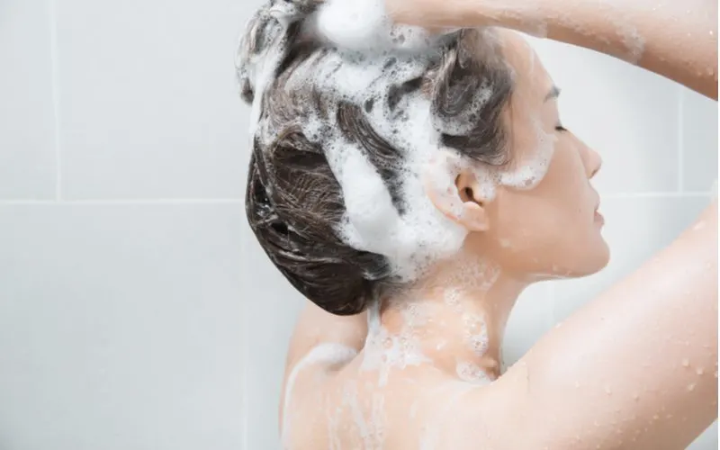 Asian woman closing her eyes while shampooing her hair in a grey tiled shower
