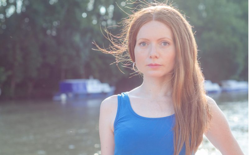 Người phụ nữ với mái tóc tĩnh lặng đứng trong chiếc áo sơ mi xanh bên ngoài cạnh hồ nước