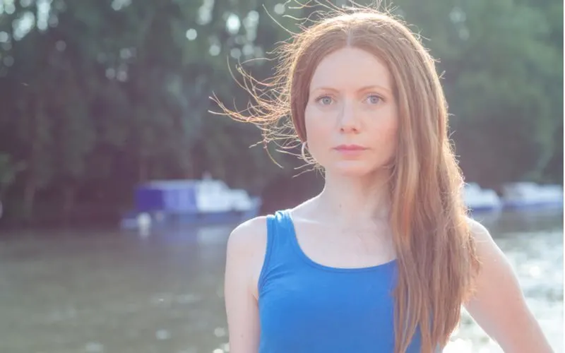 Woman with hair static stands in a blue shirt outside next to a lake