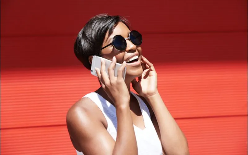 Gal with a popular black bob haircut talking on the phone and holding her other ear while standing outside