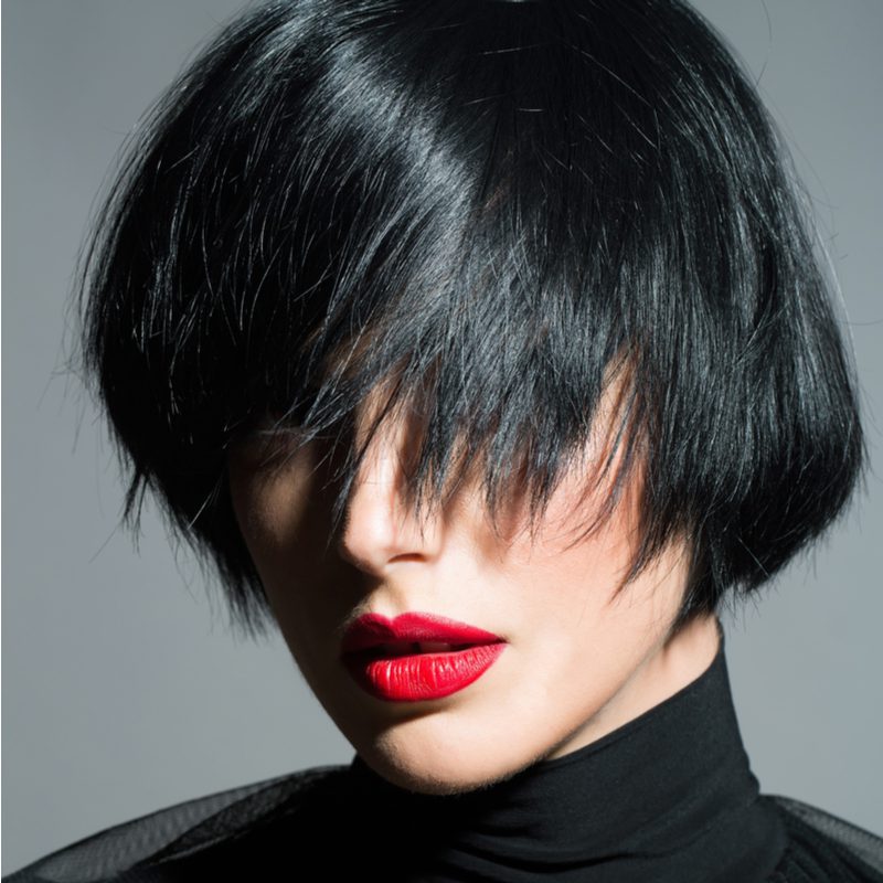 Goth chic layered bob haircut on a woman with red lips whose bangs cover her eyes and most of her nose