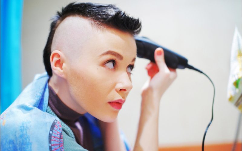 Female mohawk buzzcut on a woman giving herself a haircut looking in a mirror