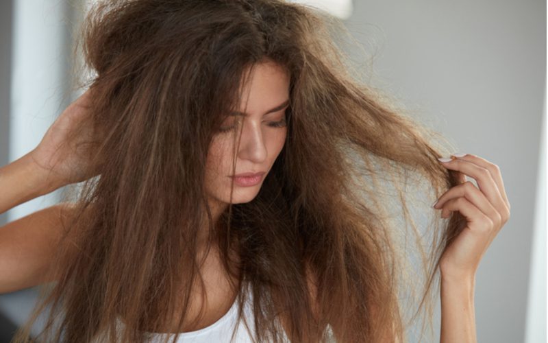 Woman with frizzy, damaged hair holding her ends for a piece on when not to get a perm