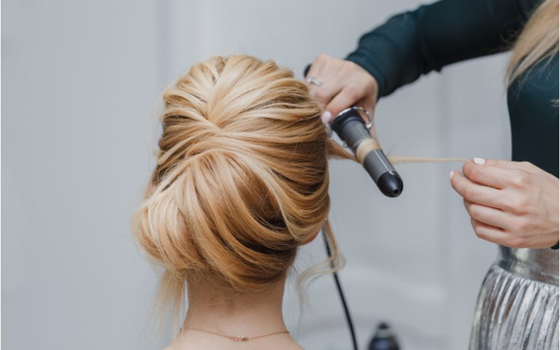 Easy updo idea titled Seamless Chignon on a woman in a salon getting her hair curled