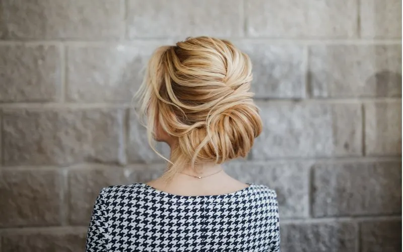 Woman with a low twist bun, a great mother of the groom hairstyle, wears a black and white patterned blouse and looks at a brick wall
