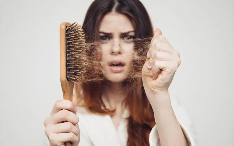 Girl pulling a bunch of long brown hair off a wooden hair brush for a piece on getting rid of greasy hair