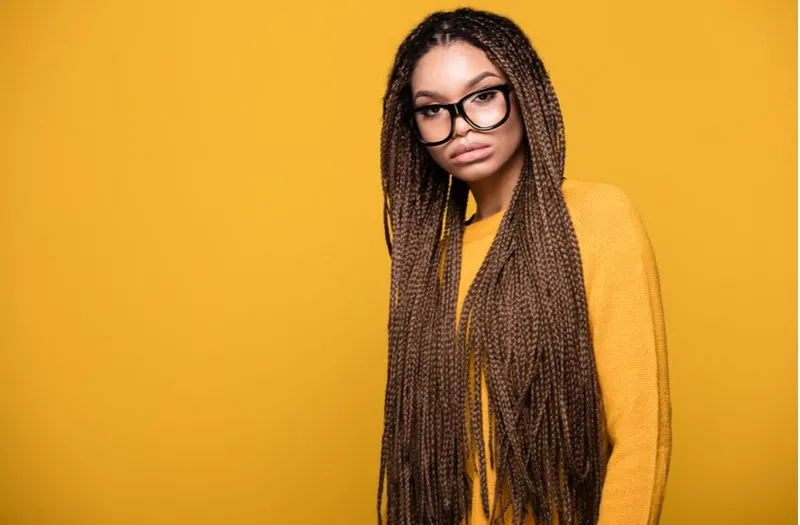 Ultra-Long Hanging Box Braids on a pretty woman in an orange sweater and black glasses