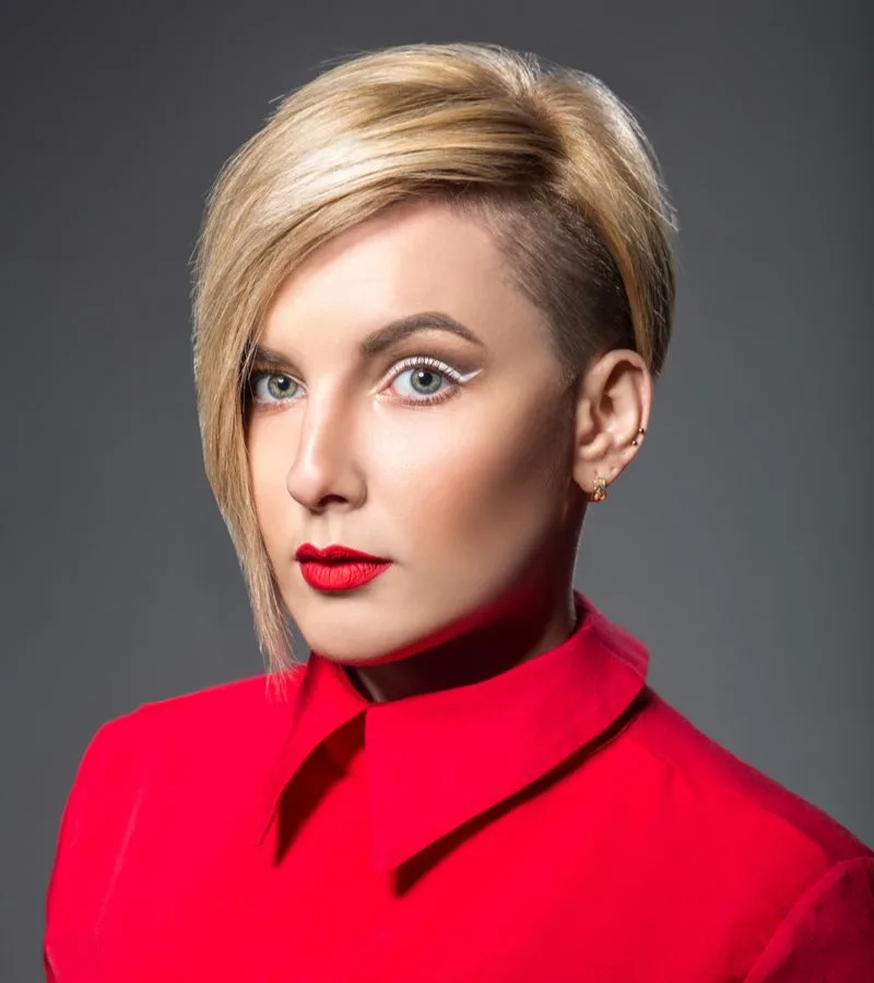 Woman with an undercut bob with really long bangs wears a red blazer and looks straight ahead in red lip