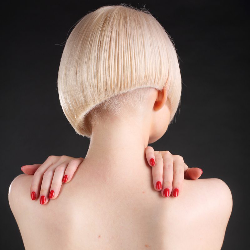 Asymmetrical bob with an undercut on a topless woman holding her shoulders wearing red nail polish