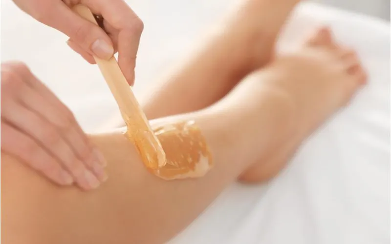 To illustrate how long hair has to be to wax, a woman rubbing wax on a leg with a wooden stick