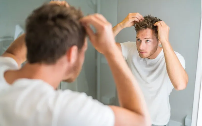 Guy styling a faux hawk while looking in the bathroom mirror and touching the spikes on his head