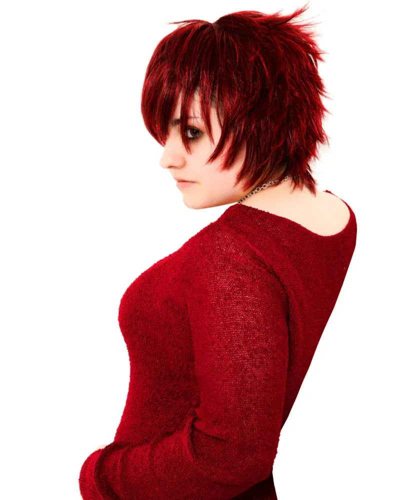 Woman with a feathered shag haircut in a red shirt puts her hand in her left pocket and leans back while looking over her left shoulder