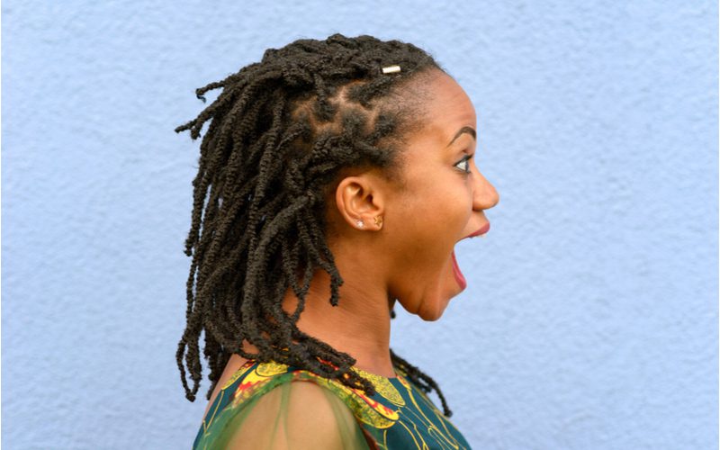 Girl with pulled-back tribal braided locs opens her mouth wide in surprise in a side profile image