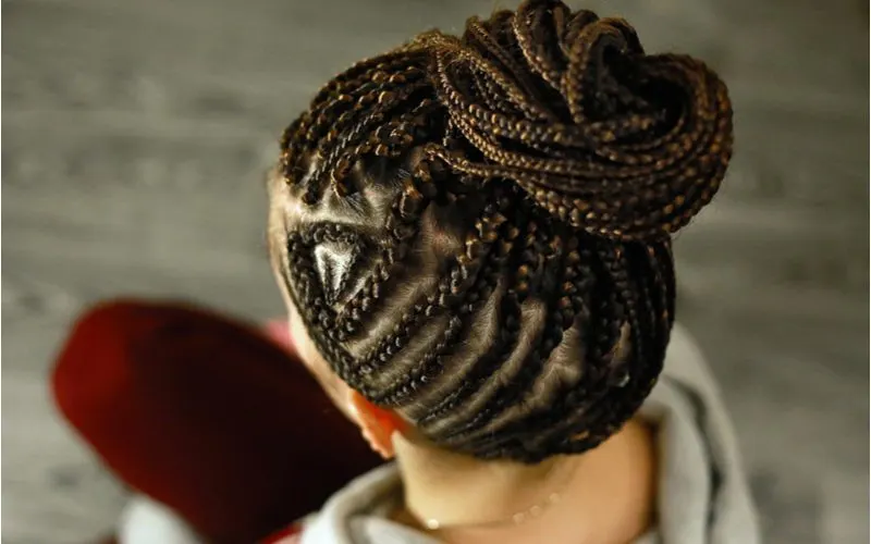 Intricately Braided Updo is one of our favorite black hairstyles on a woman sitting down on a wooden laminate flooring surface
