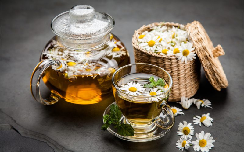 Photo of chamomile tea sitting on a table next to a big basket of flowers to help lighten hair without bleach
