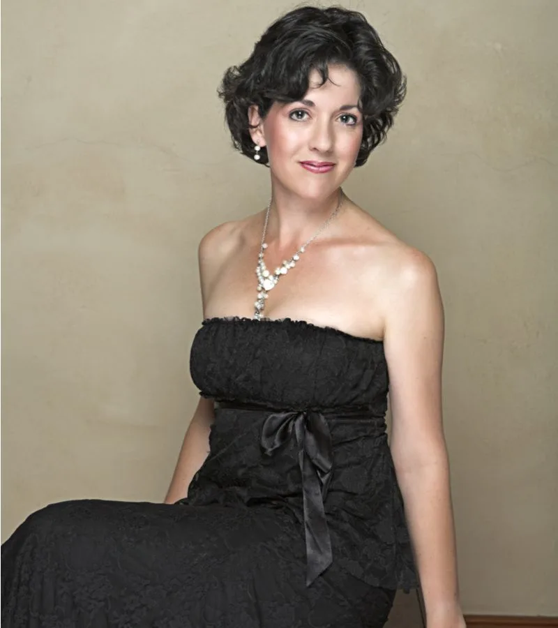 Tapered Curls and Feathered Bangs on a woman in a black dress sitting on a bench