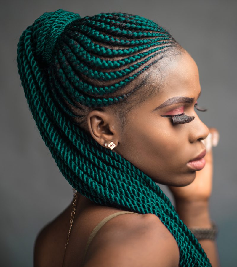 Deep jade hair color on a woman with box braids and extremely long fake eyelashes
