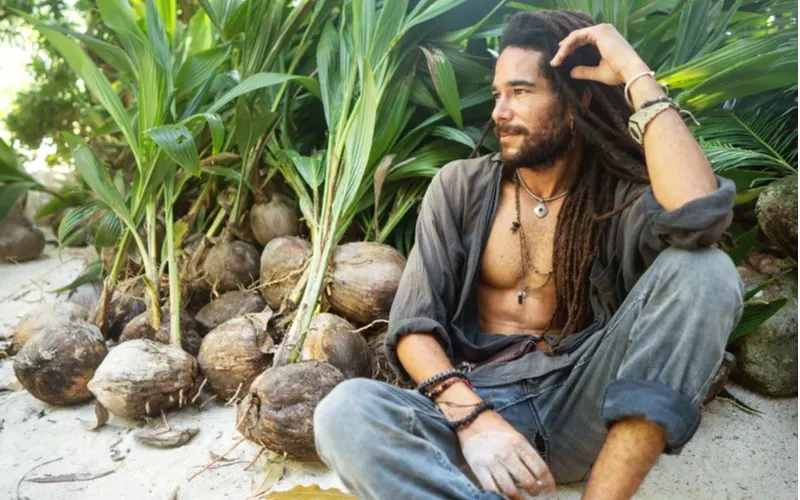 Island-aura man with wool rubbed dreadlocks hanging from his head and sitting cross-legged with his weathered collared shirt open