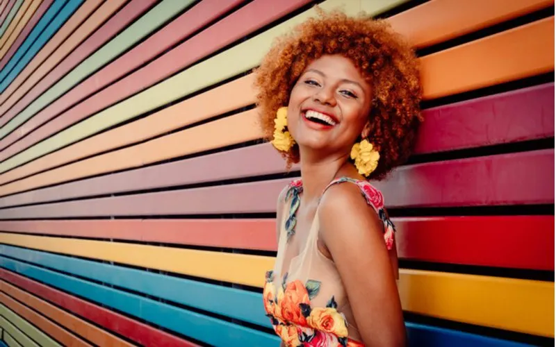 Dimensional copper hair color on a woman with light brown skin standing in front of a multi-colored wood paneled wall