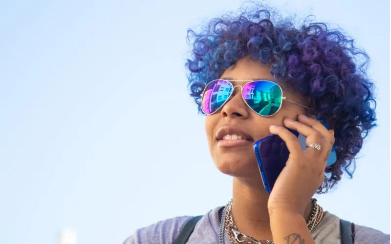 Violet blue, a favorite hair color for brown skin, on a woman talking on a smartphone with a blue case