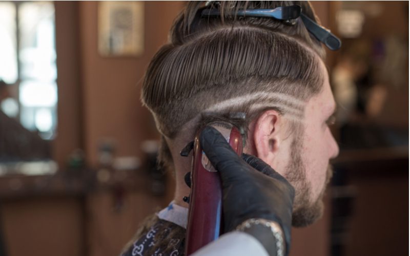 Barber cutting a hairstyle pattern into the back and sides of a guy's head