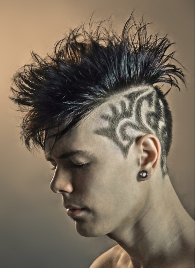 Man with a hairstyle pattern in the shape of an Aztec decoration and a mohawk looking right in a side profile image