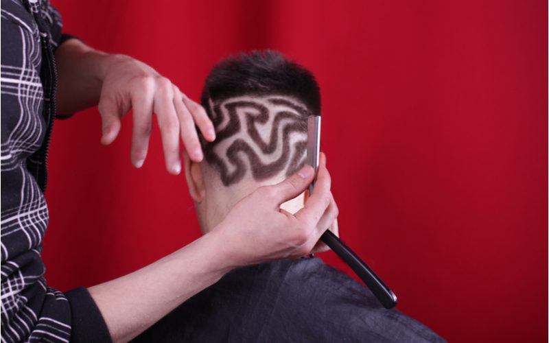 Hairstyle pattern with squiggly lines being cut with a straight razor and clippers on an asian man in a red barber shop
