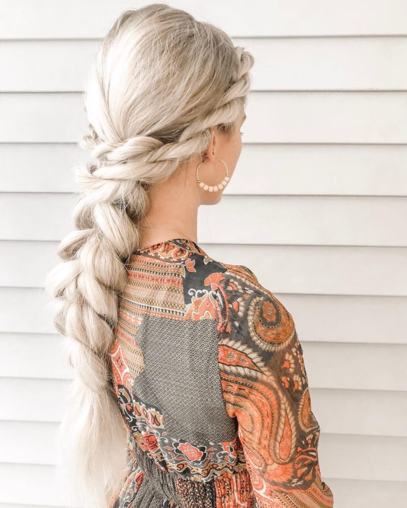 Large fishtail braid wedding guest hairstyle on a woman in a grey floral shirt