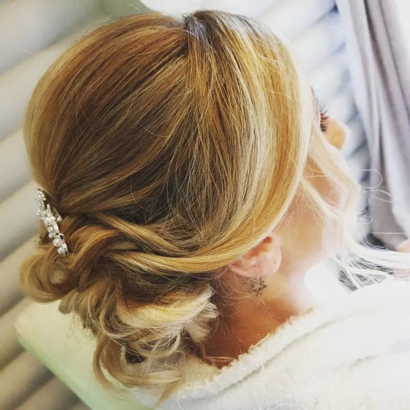 Bridesmaid updo on a blonde woman with her hair pinned back with a metal clip as viewed from the side