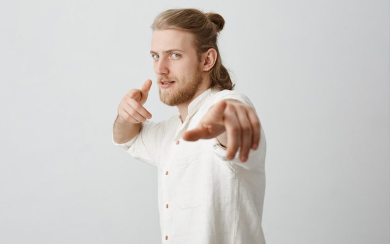 Image of a guy pointing at the camera with his finger guns while wearing a man bun