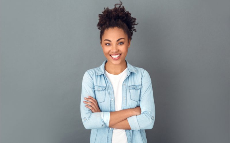 High Puff Pony displayed on a black woman crossing her arms in a jean jacket in a studio for a piece on easy hairstyles