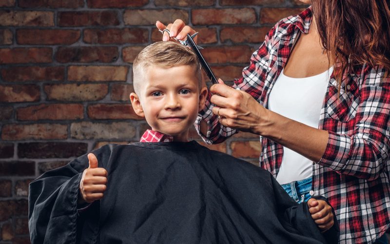 Little boy getting a haircut from a gal in a plain shirt and open white undershirt