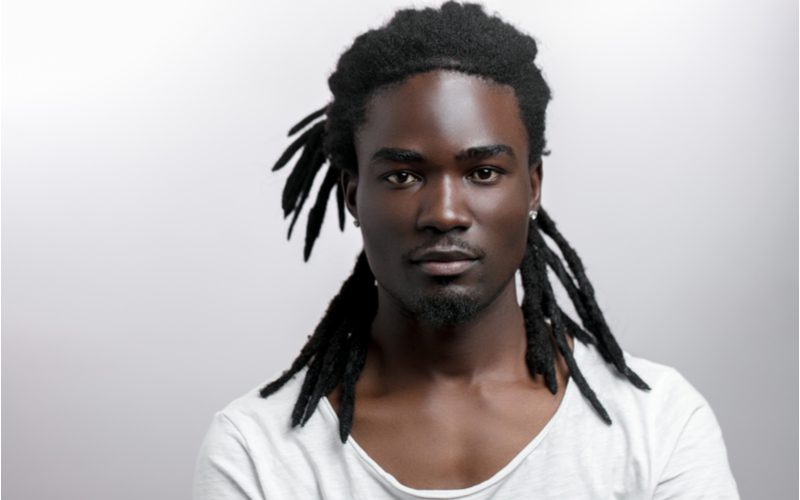 Muscular black man with half-up locs looks menacingly at the camera in a white shirt while crossing his arms 