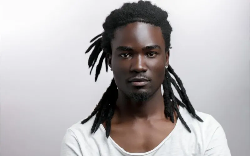 Muscular black man with half-up locs looks menacingly at the camera in a white shirt while crossing his arms 