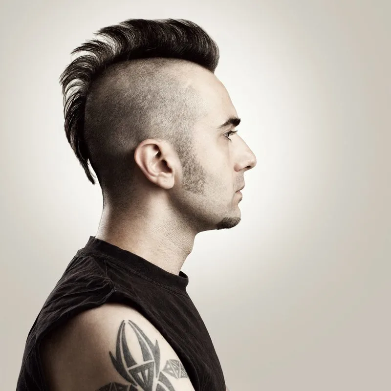Crescent Mohawk Haircut on a guy with shaved sides and wearing a black cutoff shirt that shows his tattoos