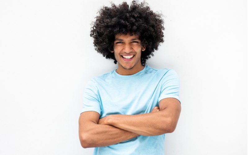 Defined and Tapered Fro, a black mens hairstyle, on a guy crossing his arms in a blue shirt