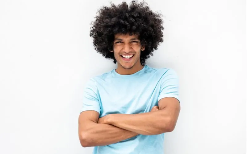 Defined and Tapered Fro, a black mens hairstyle, on a guy crossing his arms in a blue shirt