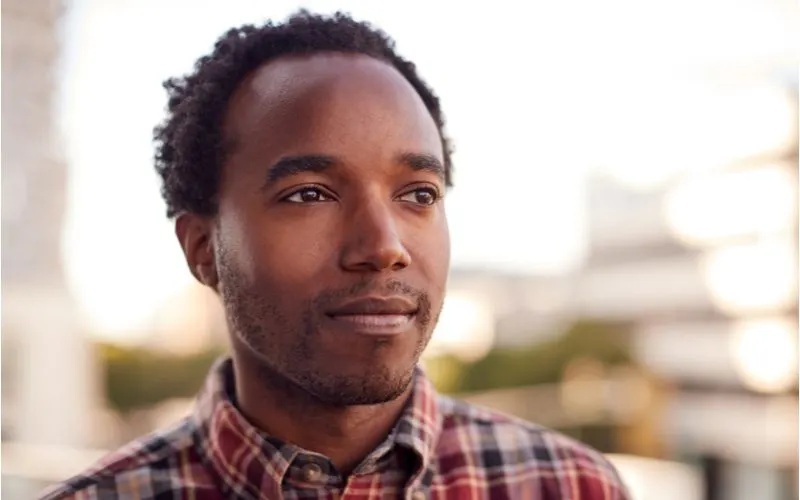 Black male hairstyle inspiration with a Medium-Short Natural Curls cut worn by a handsome and content looking black male