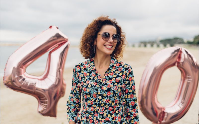 For a piece on best hairstyles for women over 40, a gal in glasses stands on the beach between balloons that spell out 40