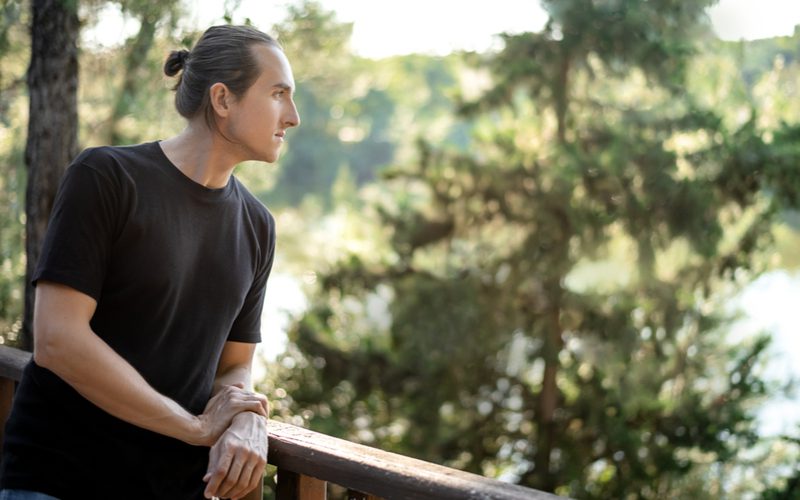 Neat Midi Man Bun on a guy leaning on a railing and looking a nature preserve