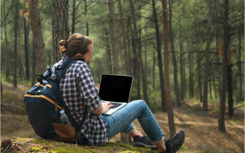 Man in a plaid shirt sitting outdoors working on a laptop wearing a Mid Looped Man Bun With Headband