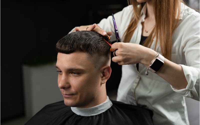 Caesar Crop haircut for a receding hairline getting trimmed by a woman in a white jacket and shears