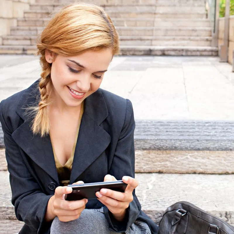 Woman wearing an easy hanging side braid (a great and easy long to medium length hairstyle) while looking at her phone