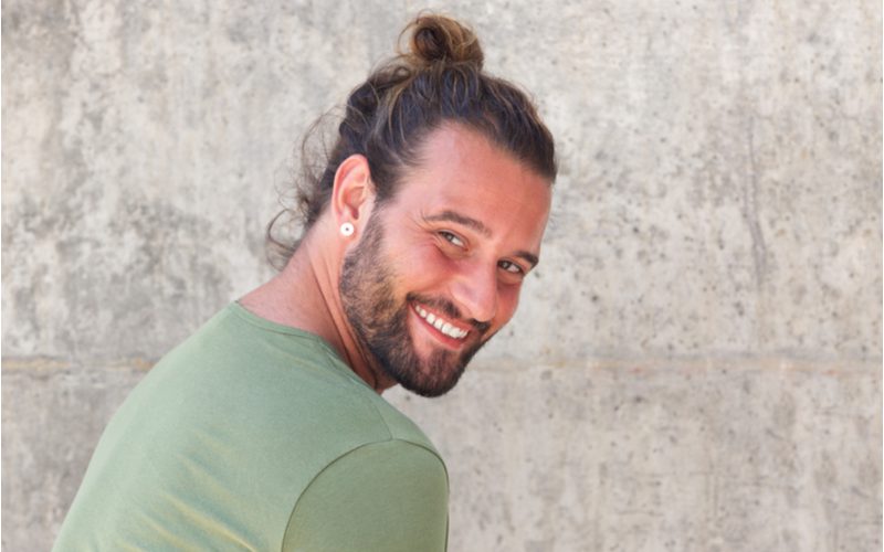 Messy and Casual Looped Man Bun on a guy smiling over his shoulder in a grey room
