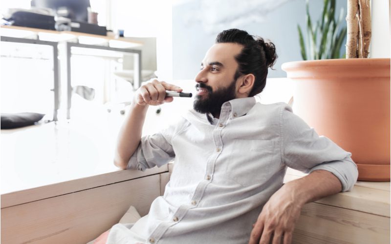 High-Volume Boosted Man Bun worn by a guy in a white button-up leaning against the back of a tan couch