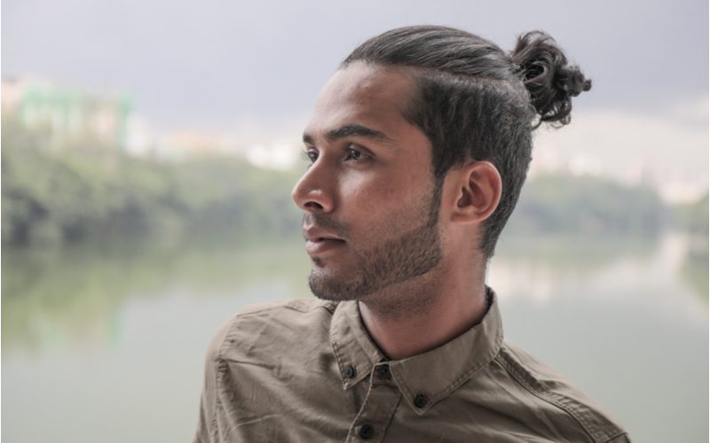 Half Up With Shaved Sides man bun on a slightly asian-looking man standing in front of a river