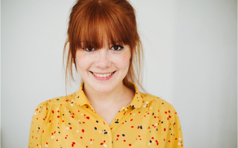 Wispy Full Fringe types of bangs on a gal in a yellow speckled shirt wearing freckles and red hair